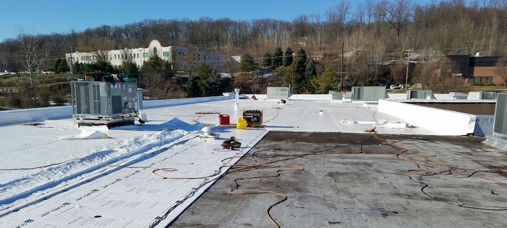 A white, single-ply membrane being installed to reduce commercial roofing costs.